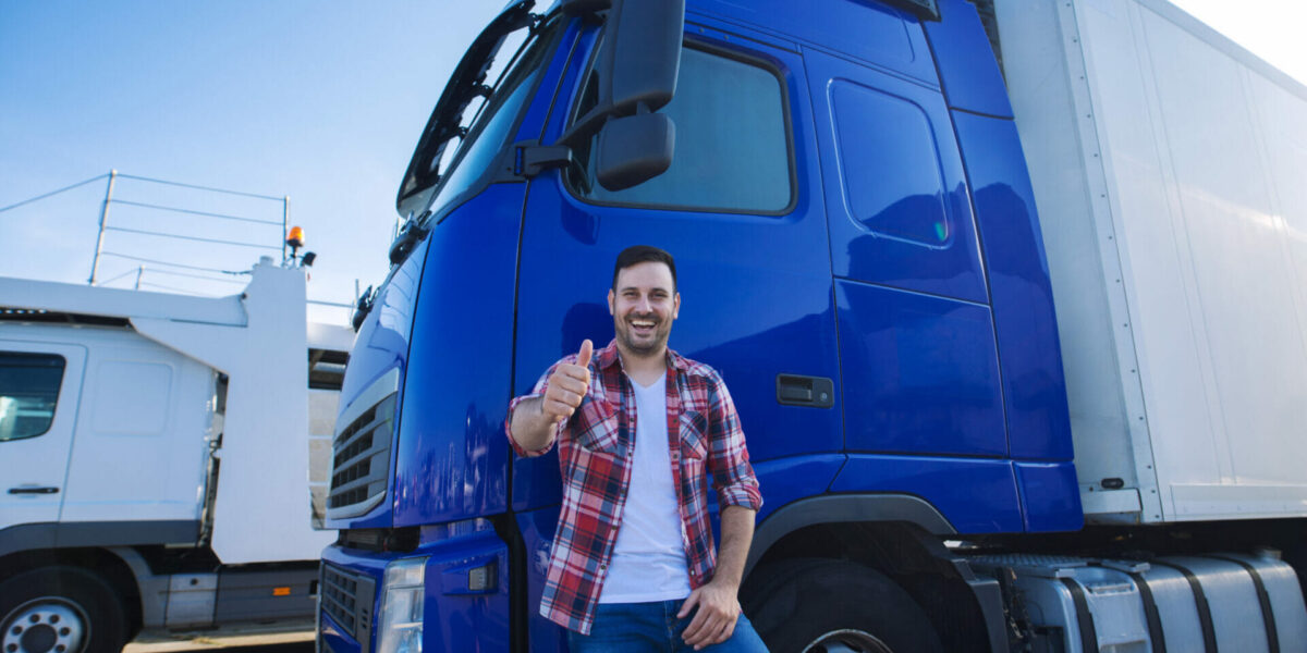 Professional truck driver in front of long transportation vehicle holding thumbs up ready for a new ride.